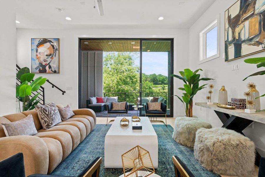Spacious living room showcasing recessed lighting, wide-plank flooring, and seamless indoor-outdoor flow to the covered balcony.