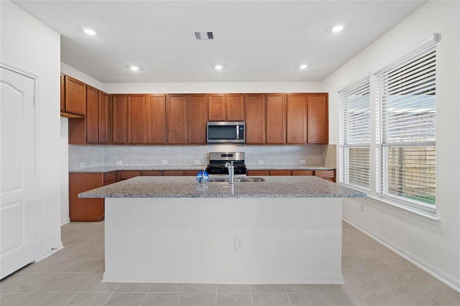 This spacious kitchen features high ceilings, stained wood cabinets, granite countertops, SS appliances, modern tile backsplash, recessed lighting, large kitchen island with space for a breakfast bar, large windows with privacyt blinds, and a pantry all overlooking your dining room and huge family room.