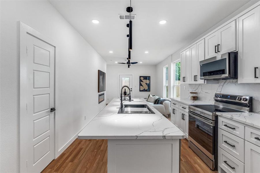 Kitchen featuring stainless steel appliances, white cabinetry, a kitchen island with sink, light wood-style floors, and recessed lighting Kitchen featuring stainless steel appliances, white cabinetry, a kitchen island with sink, light wood-style floors, and recessed lighting