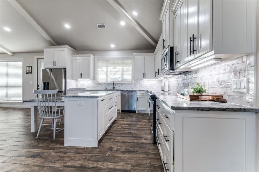 Kitchen featuring a kitchen island, white cabinetry, decorative backsplash, a kitchen bar, and appliances with stainless steel finishes
