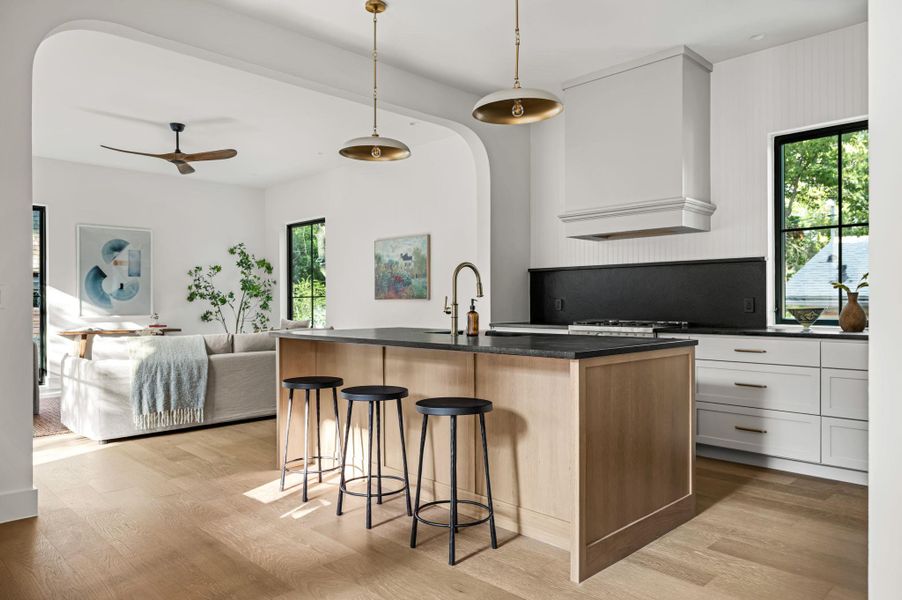A well-lit kitchen with natural light, featuring a generous island and modern appliances, seamlessly connects to an inviting living area.