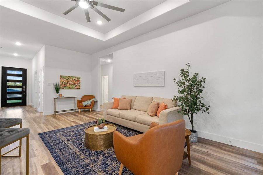 Living room with a raised ceiling, hardwood / wood-style floors, and ceiling fan