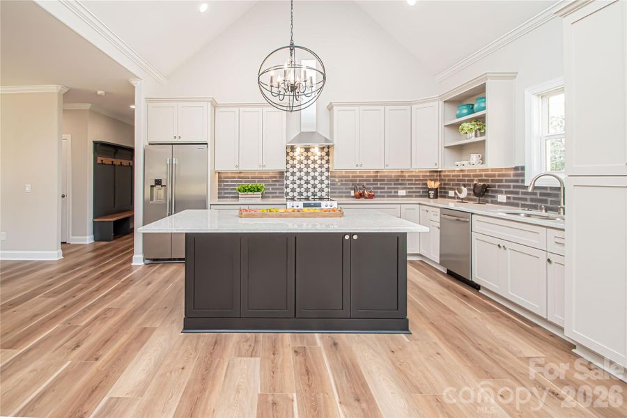 This stunning kitchen with vaulted ceilings showcases stainless steel appliances, granite countertops, a stylish gray subway tile backsplash, and soft-close cabinetry with convenient pull-out drawers.