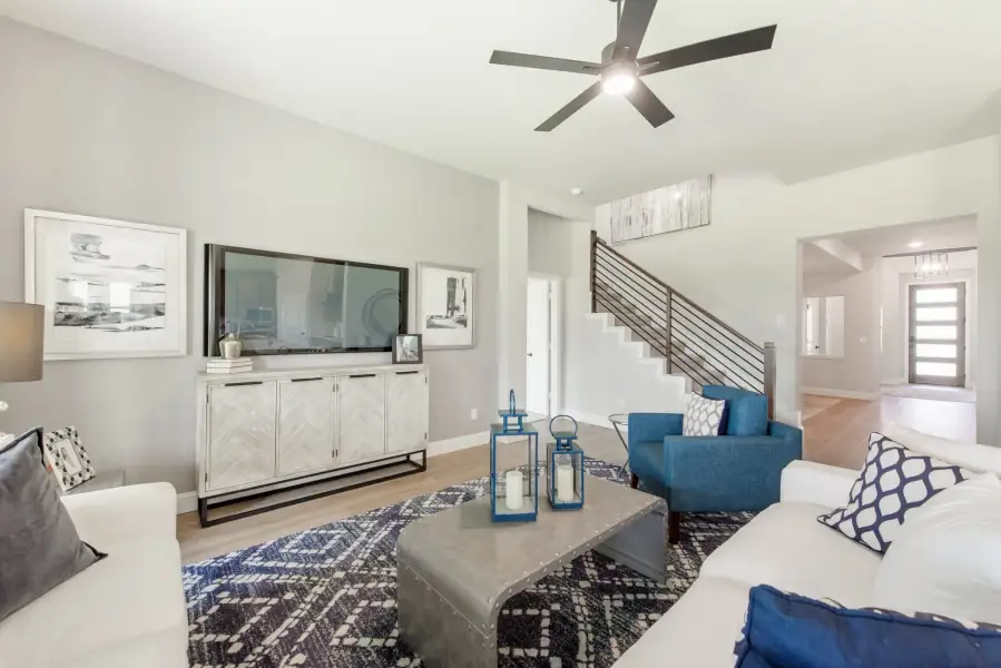 Living room with white sofa, blue accent chairs, large TV, and staircase with metal railing