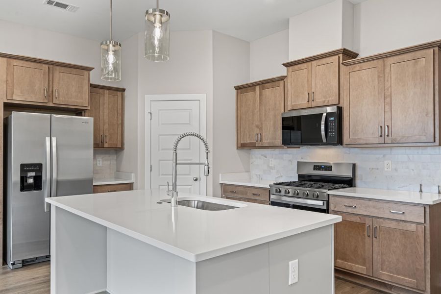 Kitchen featuring stainless steel appliances, tasteful backsplash, pendant lighting, a center island with sink, and brown cabinetry