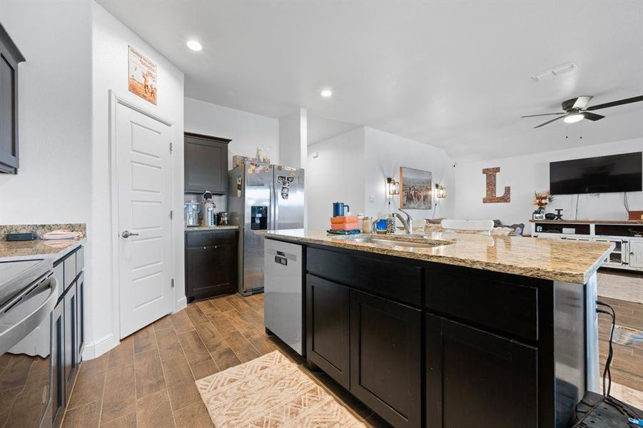Kitchen with wood finish floors, stainless steel appliances, light stone counters, an island with sink, and ceiling fan Kitchen with wood finish floors, stainless steel appliances, light stone counters, an island with sink, and ceiling fan