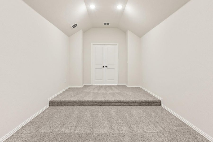 Empty room with vaulted ceiling, gray carpet, raised platform, and white double doors
