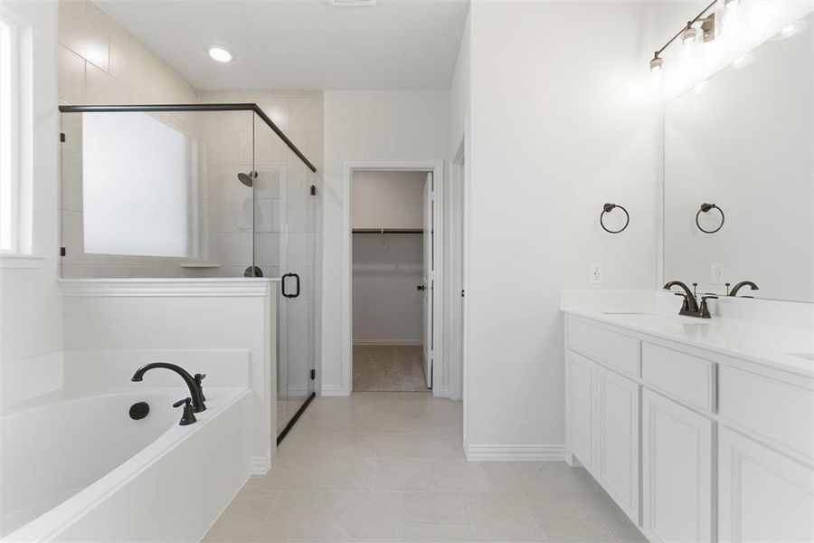 Bathroom with a bath, double vanity, a spacious closet, a stall shower, and light tile patterned floors