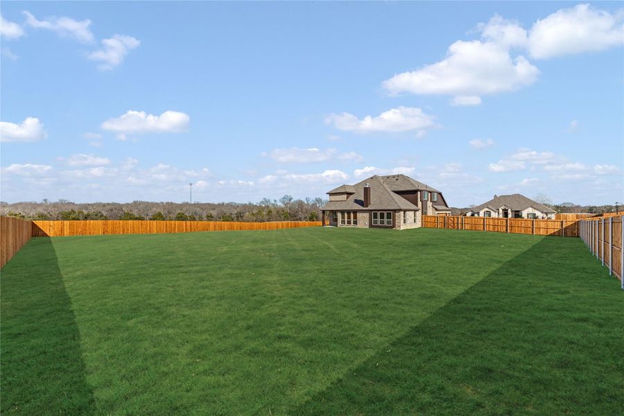 Large backyard with green lawn, wood privacy fence, and two-story brick home in background Large backyard with green lawn, wood privacy fence, and two-story brick home in background