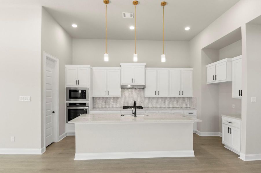 Kitchen with hanging light fixtures, backsplash, white cabinetry, light stone counters, and stainless steel oven Kitchen with hanging light fixtures, backsplash, white cabinetry, light stone counters, and stainless steel oven