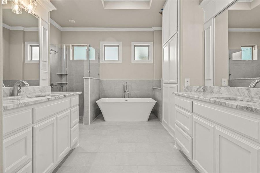Bathroom with plenty of natural light, ornamental molding, two vanities, tile walls, and a freestanding tub