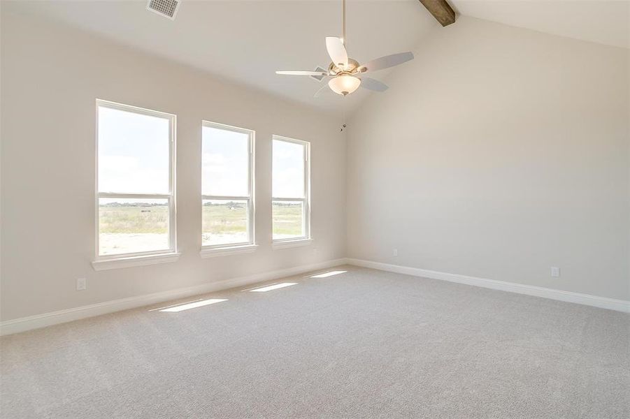 Carpeted empty room featuring beam ceiling, a wealth of natural light, ceiling fan, and high vaulted ceiling