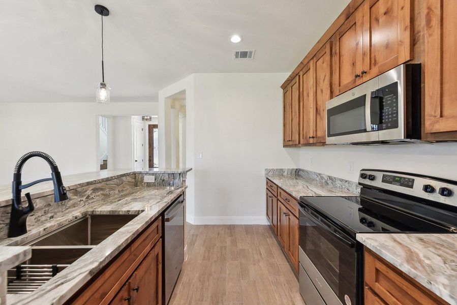 Kitchen with brown cabinetry, visible vents, light wood-style flooring, a sink, and appliances with stainless steel finishes