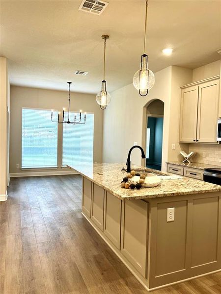 Kitchen with a sink, arched walkways, wood finished floors, an island with sink, and white microwave Kitchen with a sink, arched walkways, wood finished floors, an island with sink, and white microwave