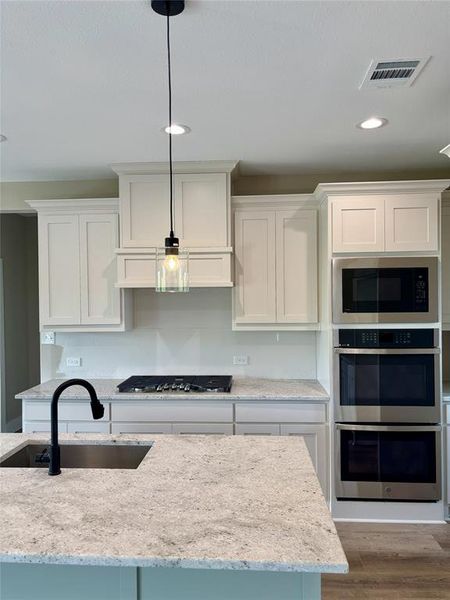 Kitchen with light stone countertops, stainless steel appliances, white cabinets, and decorative light fixtures