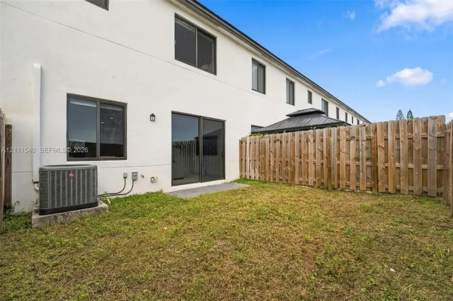 Rear exterior featuring smooth stucco siding, sliding glass doors, and a private wooden fence