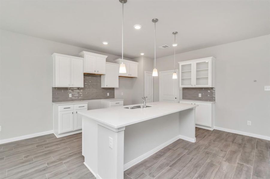 This modern kitchen is a chef's delight, featuring sleek white cabinetry, an expansive island with a built-in sink, and stylish pendant lighting that adds a touch of elegance. The clean lines and neutral tones create a fresh, airy ambiance, perfect for both cooking and entertaining. With ample storage and counter space, this kitchen is as functional as it is beautiful. **This image is from another Saratoga Home with similar floor plan and finishes, not the June floorplan.**