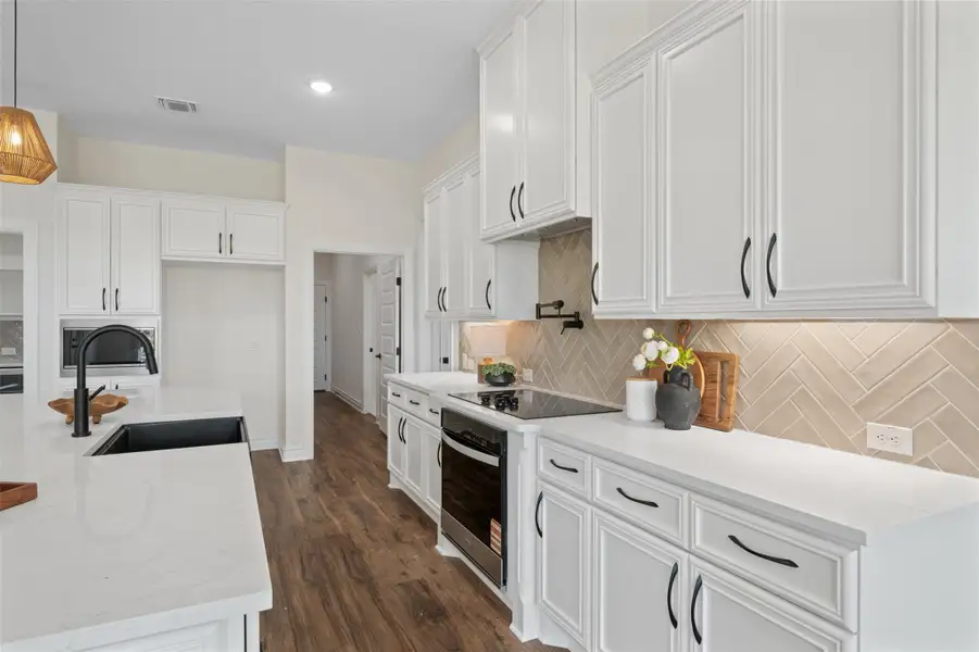 Kitchen with white cabinetry, hanging light fixtures, light stone counters, decorative backsplash, and black appliances Kitchen with white cabinetry, hanging light fixtures, light stone counters, decorative backsplash, and black appliances