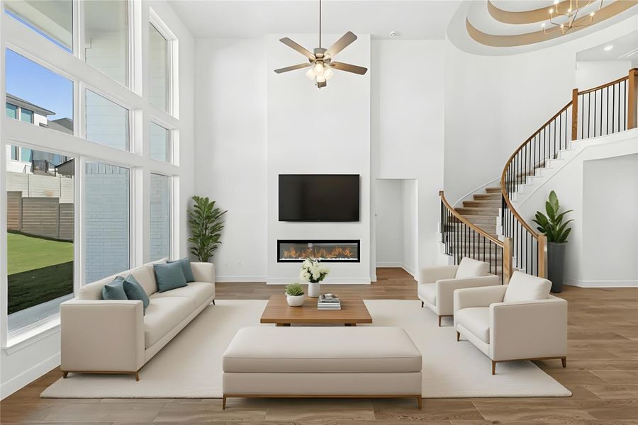 Living room featuring a glass covered fireplace, stairway, wood finished floors, a ceiling fan, and a high ceiling