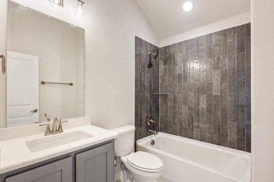 Bathroom with gray vanity, white countertop, and tub-shower combo with dark tile surround Bathroom with gray vanity, white countertop, and tub-shower combo with dark tile surround