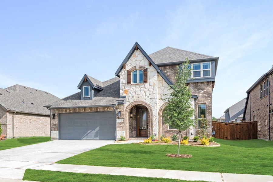 Two-story home with stone and brick exterior, two-car garage, arched entry, and landscaped front yard