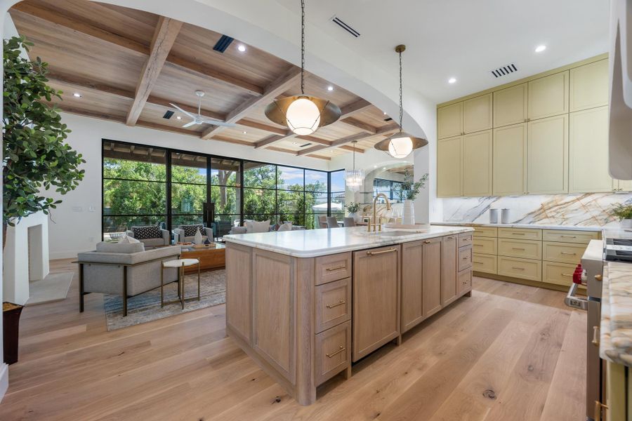 An arched opening connects the open kitchen to a living area with wood ceiling beams.