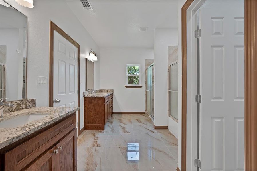 Bathroom featuring a shower stall, two vanities, and marble finish flooring