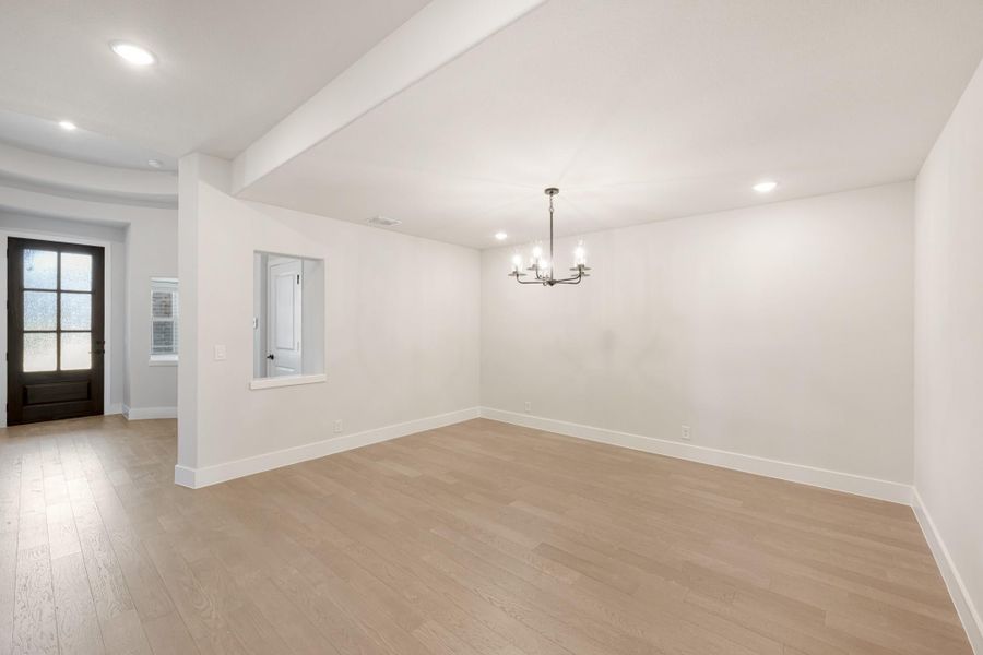 Empty dining room with light hardwood floors, chandelier, white walls, and view to front entry door.