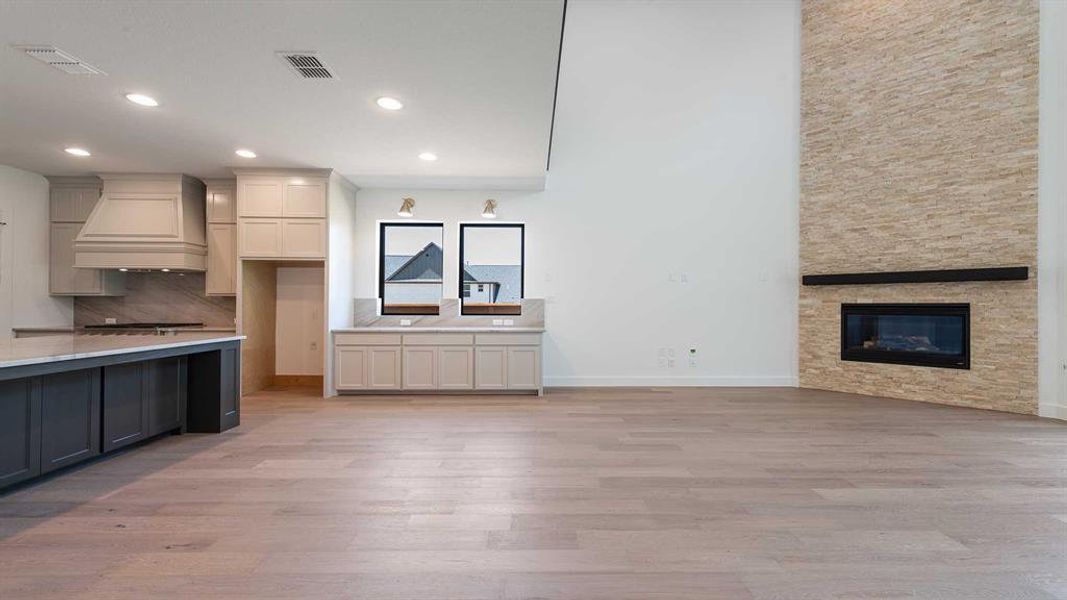 Kitchen with custom range hood, recessed lighting, light wood-style flooring, decorative backsplash, and a fireplace