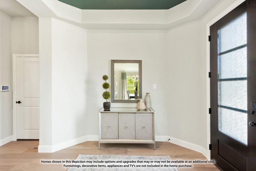 Home entryway with tray ceiling, dark front door with glass panels, console table, wall mirror, and light hardwood floors Home entryway with tray ceiling, dark front door with glass panels, console table, wall mirror, and light hardwood floors