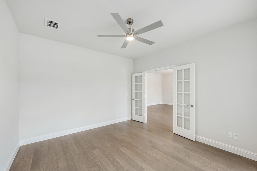 Empty room with hardwood floors, ceiling fan, and open French doors leading to adjacent space Empty room with hardwood floors, ceiling fan, and open French doors leading to adjacent space