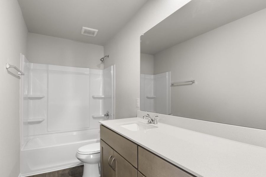 Image of a bathroom with a large mirror, a dual white vanity, white shower and tub, and light brown cabinets