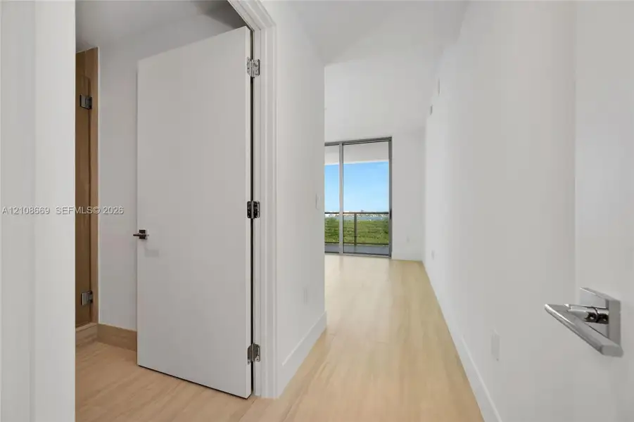 Interior space featuring wood-finish flooring, white walls, flush-panel doors, modern lever-style hardware, and floor-to-ceiling sliding glass doors