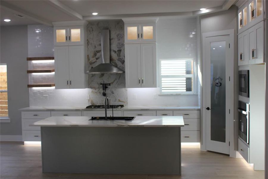 Kitchen featuring light hardwood / wood-style floors, white cabinets, range hood, and an island with sink