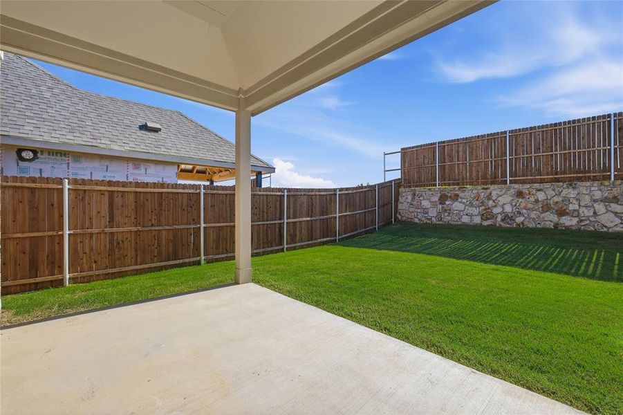 Expansive backyard featuring a covered concrete patio, verdant lawn, and a privacy fence