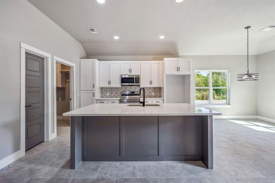 Kitchen featuring white cabinetry, appliances with stainless steel finishes, vaulted ceiling, and sink