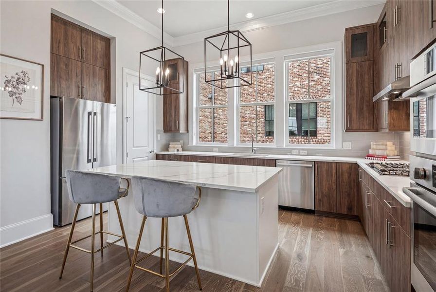 Kitchen featuring a central island with a white countertop, wood-finish flooring, stainless steel appliances, dark wood cabinetry, and three large windows