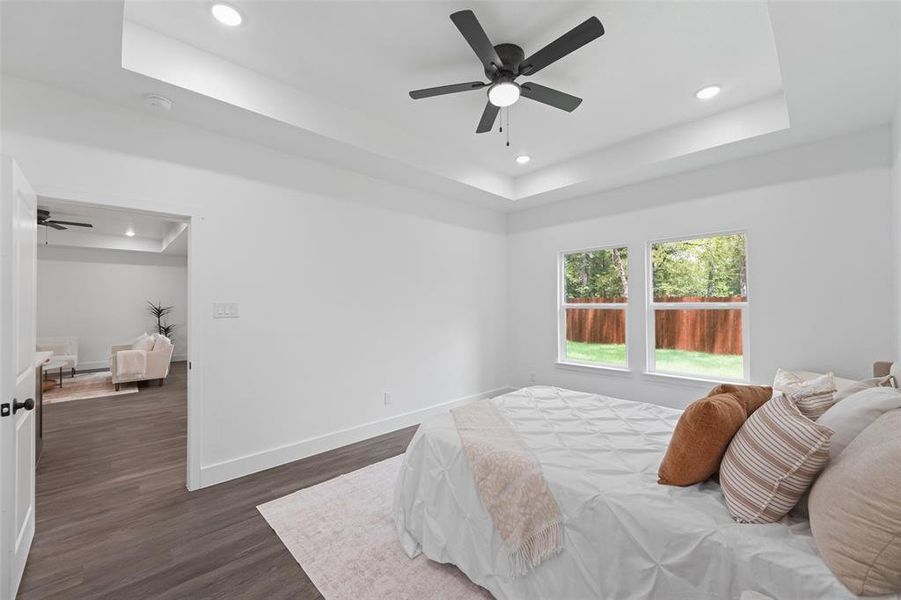 Room featuring wood-finish flooring, a tray ceiling with recessed lighting, and a ceiling fan Room featuring wood-finish flooring, a tray ceiling with recessed lighting, and a ceiling fan