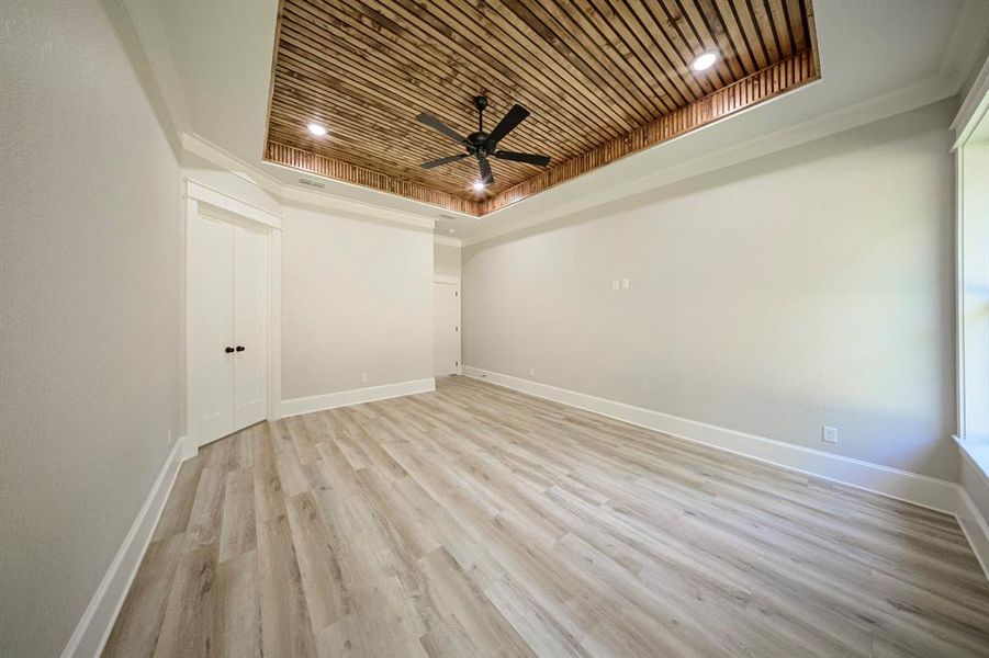 Empty room with light wood-style floors, wood ceiling, a raised ceiling, ceiling fan, and crown molding Empty room with light wood-style floors, wood ceiling, a raised ceiling, ceiling fan, and crown molding