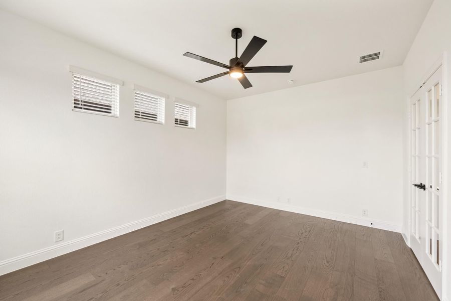 Empty room with dark hardwood floors, white walls, ceiling fan, and French doors