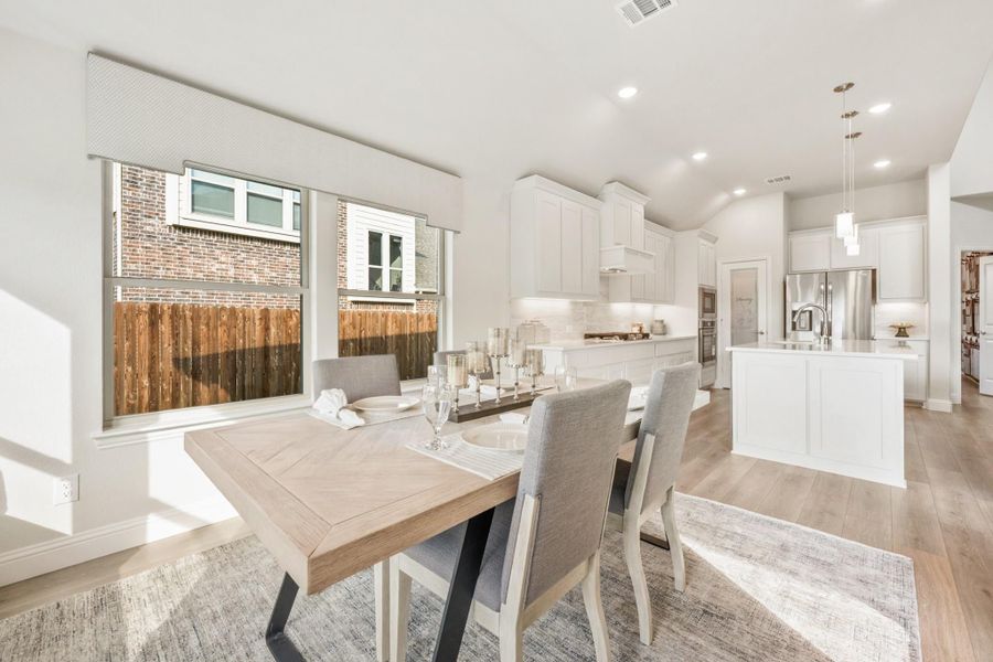 Open dining area with wood table flowing into white kitchen with island and hardwood floors Open dining area with wood table flowing into white kitchen with island and hardwood floors