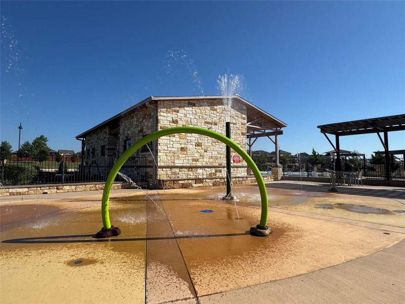 Splash pad with integrated water features, concrete surfacing, and a stone-clad building