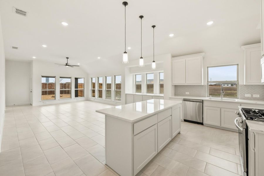 Open kitchen with white cabinets, center island, pendant lights, and stainless steel appliances open to living area