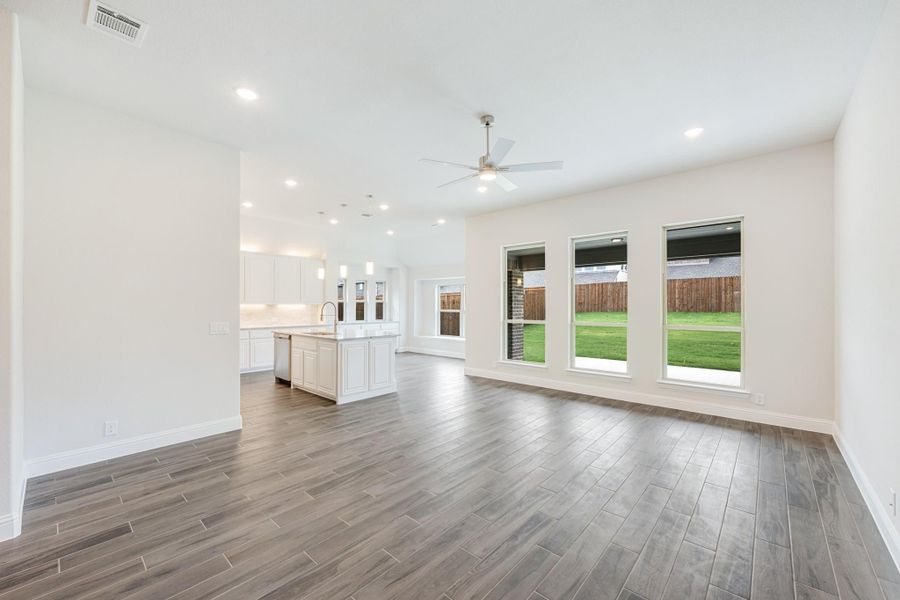 Open living area with wood-look floors and ceiling fan, open to kitchen with white cabinets and island