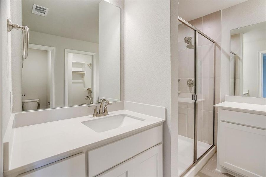 Bathroom featuring a shower stall, a textured wall, vanity, and a walk in closet Bathroom featuring a shower stall, a textured wall, vanity, and a walk in closet
