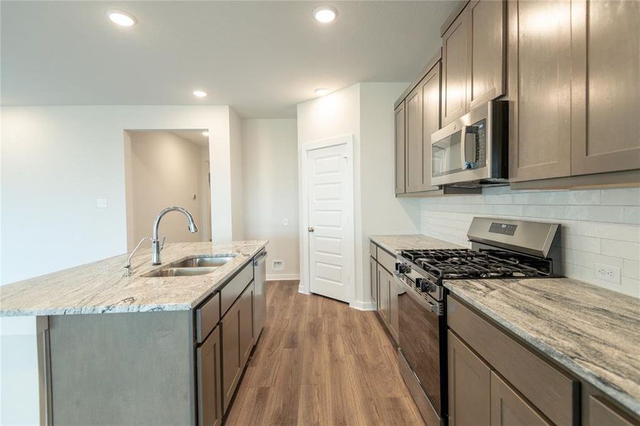 A spacious kitchen featuring a free-standing gas range, a stainless steel interior dishwasher with sanitize function, and beautiful granite countertops