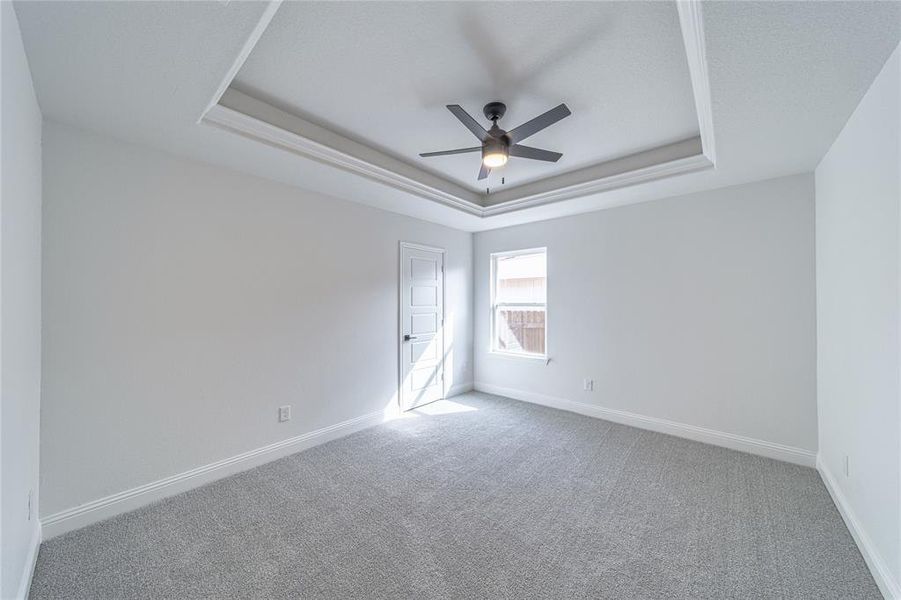 Carpeted empty room with ceiling fan, baseboards, and a raised ceiling