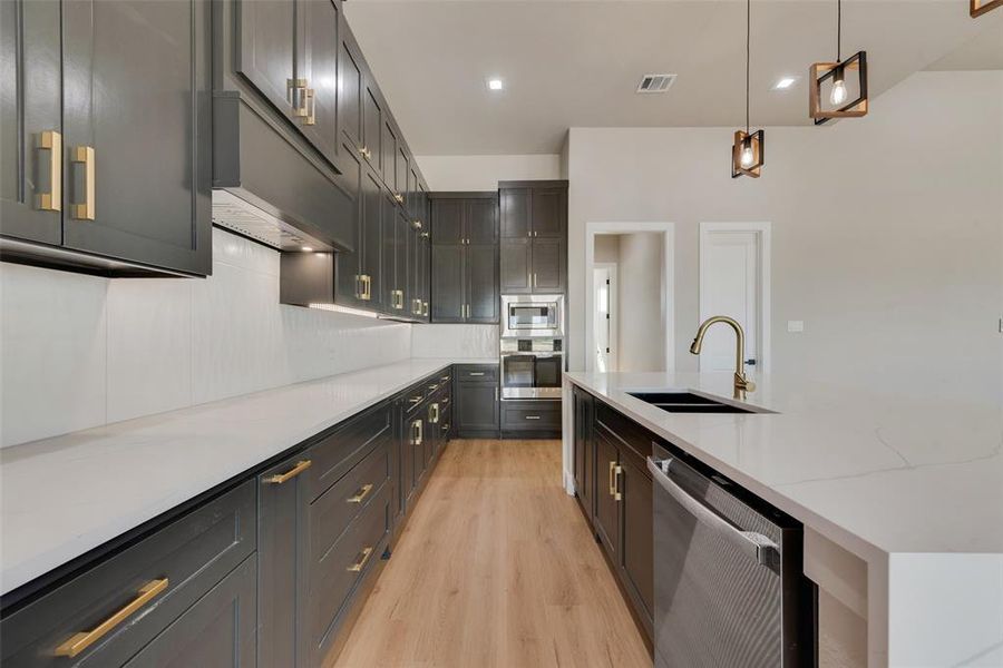 Kitchen with stainless steel appliances, light hardwood / wood-style floors, decorative light fixtures, tasteful backsplash, and sink