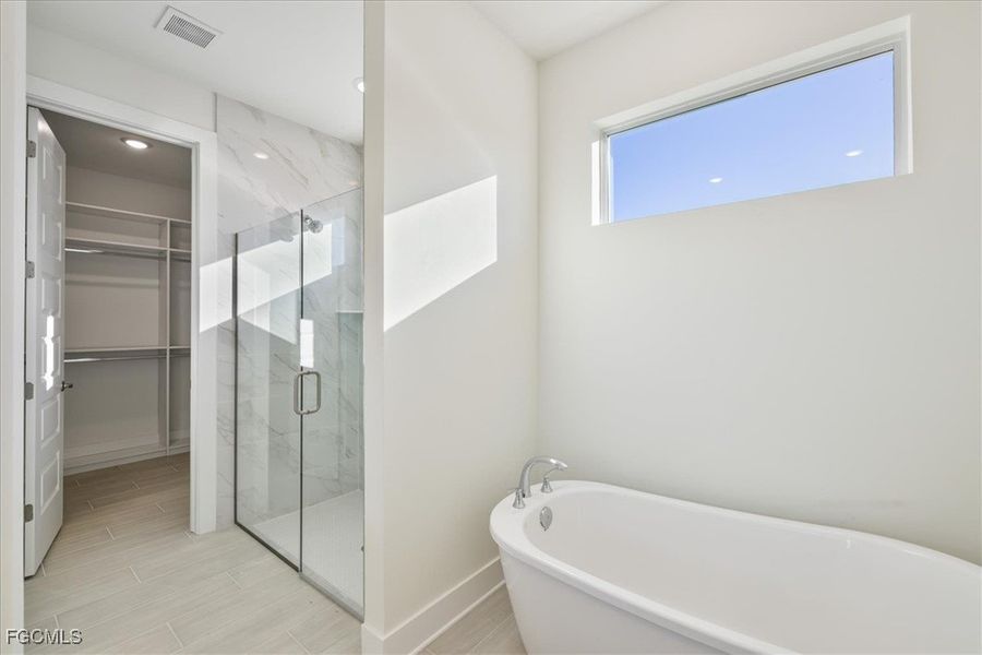 Bathroom featuring a soaking tub, a marble finish shower, and a spacious closet