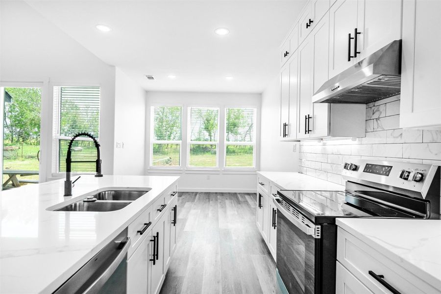 A contemporary kitchen features bright white cabinetry, sleek appliances, and durable hardwood flooring. A contemporary kitchen features bright white cabinetry, sleek appliances, and durable hardwood flooring.